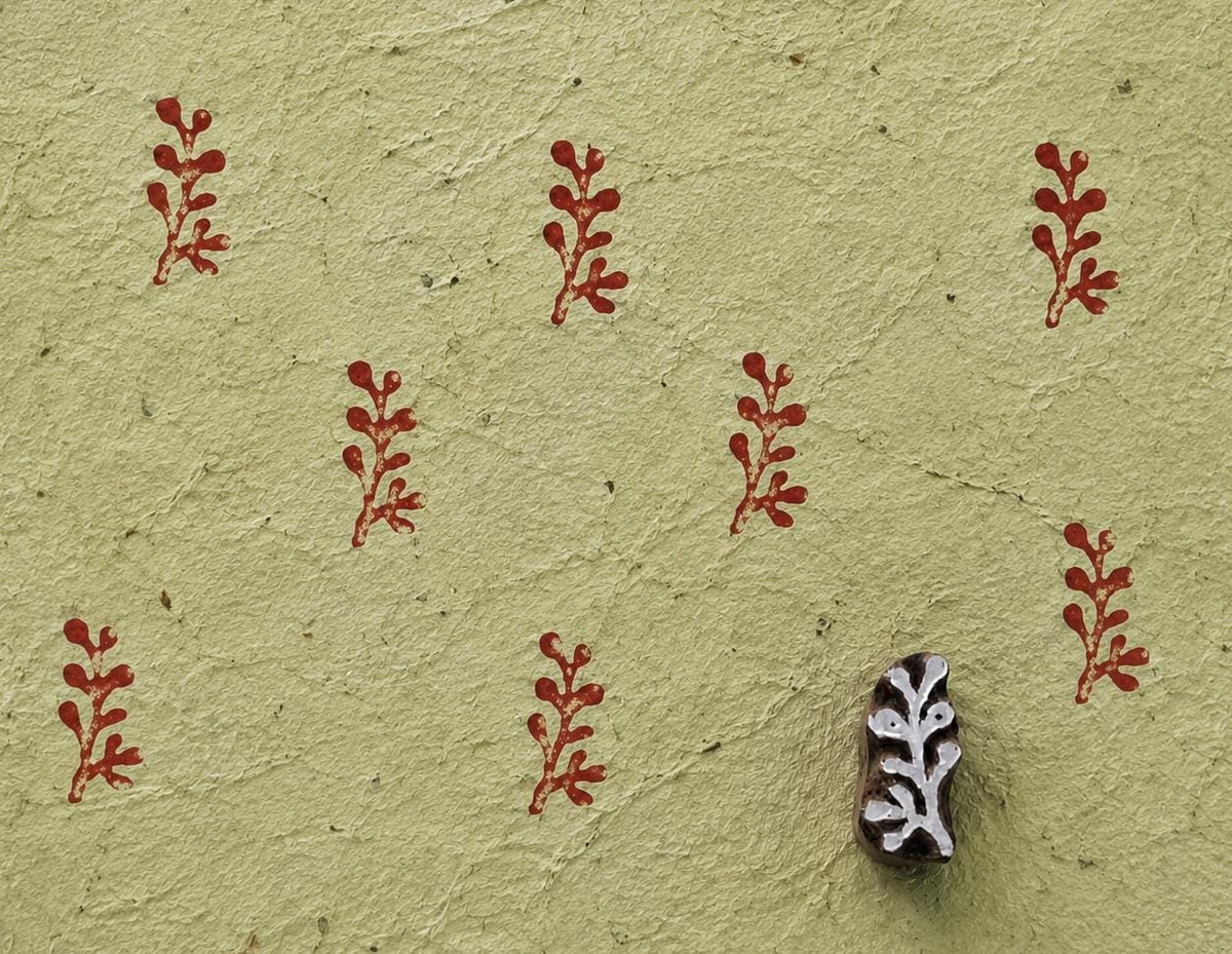 Hand carved wooden printing block measuring approximately 2.7 × 1.6 cm, featuring an unusual coral-like branching motif, shown with repeated red impressions on textured handmade paper.