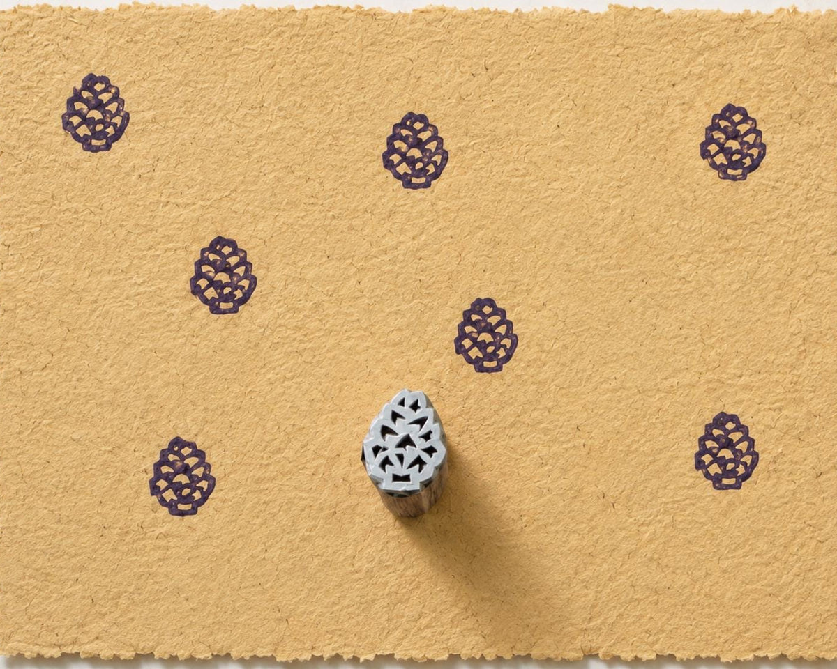 Hand carved pinecone wooden printing block stamped repeatedly in purple ink on handmade golden paper