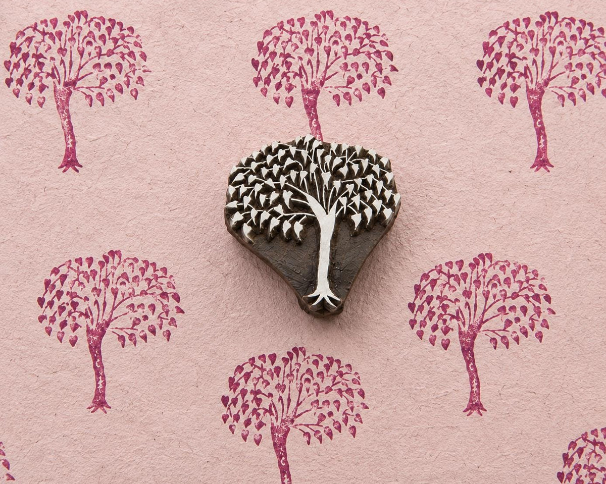 Hand carved leafy canopy wooden printing block surrounded by repeated botanical tree impressions on textured pink handmade paper.