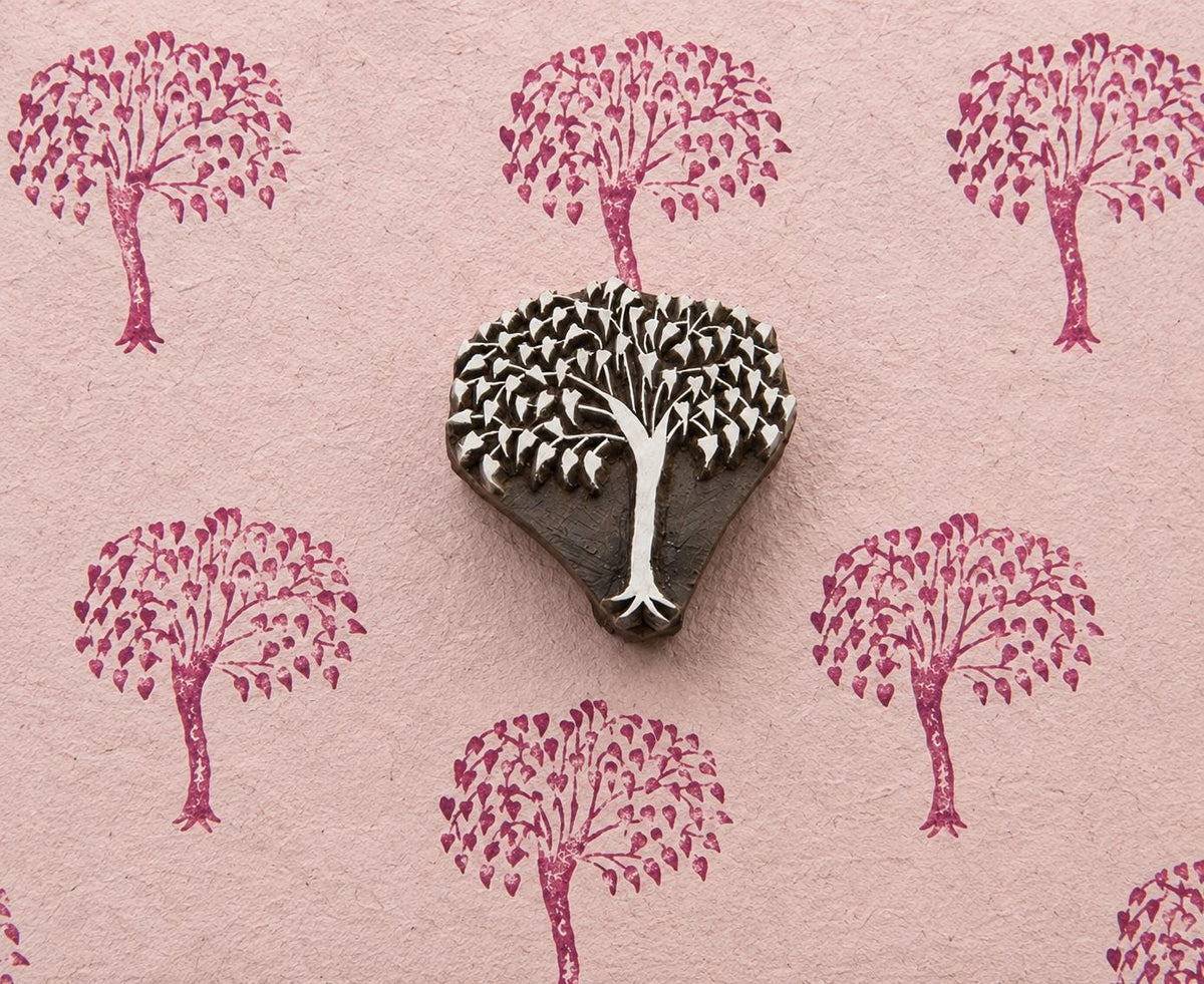 Hand carved leafy canopy wooden printing block surrounded by repeated botanical tree impressions on textured pink handmade paper.