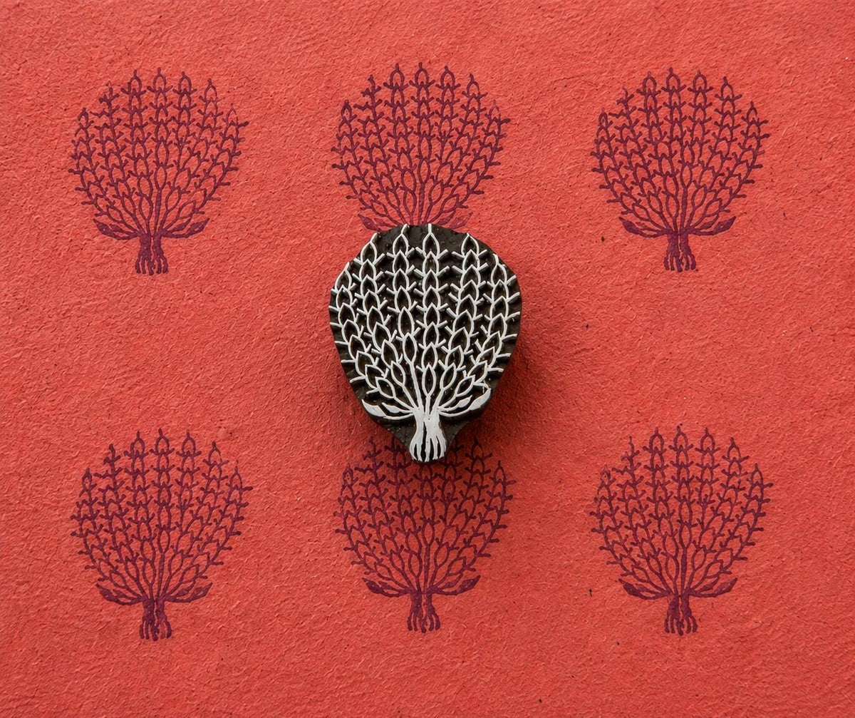 Hand carved wooden Lace Tree stamp shown with repeated dark purple tree impressions on textured red handmade paper.