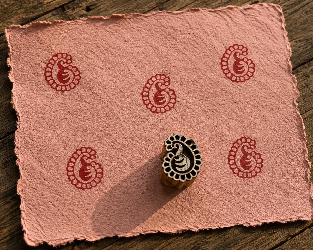 Hand carved Petite Paisley wood block stamp with deep red paisley print on handmade paper for fabric printing, pottery, clay and paper crafts.