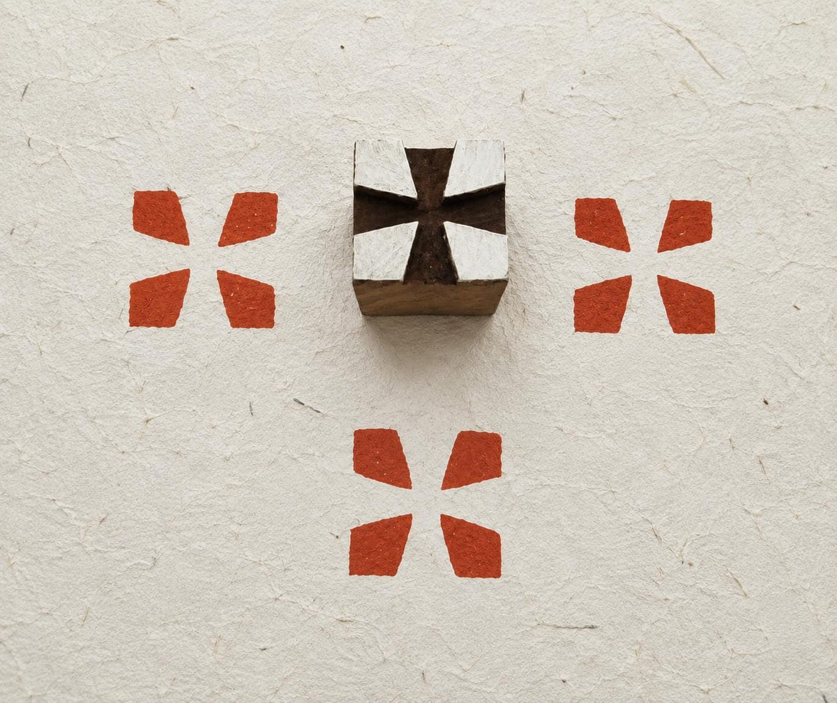 Hand carved Indian wooden fabric printing block featuring a minimalist four-petal geometric design with printed impressions on handmade paper.