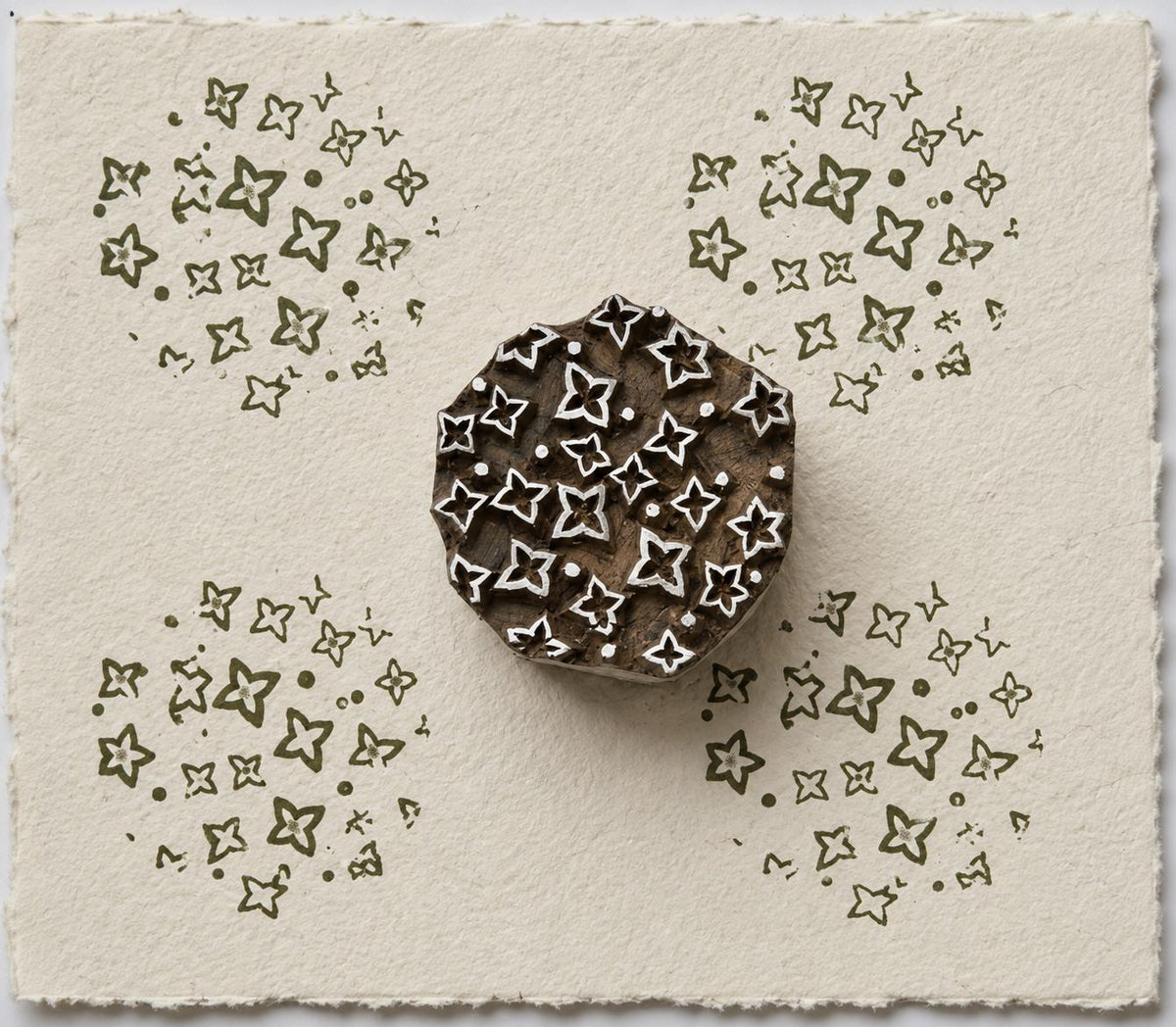 Hand carved Indian wooden printing block with a scattered folk motif of small floral and geometric shapes, shown printed on handmade paper.
