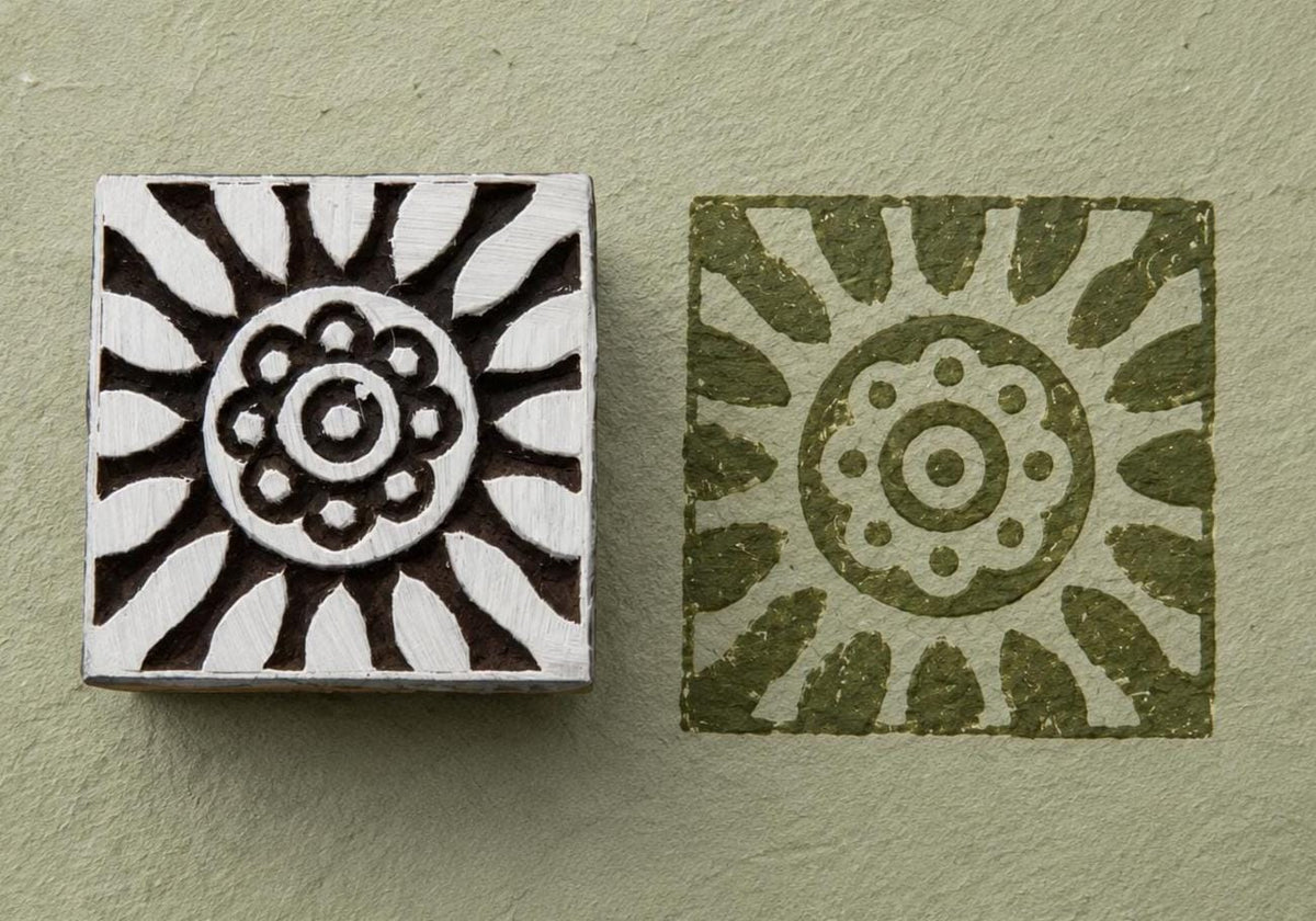 Hand carved Sunburst Flower wood stamp beside its green floral impression on textured handmade paper.