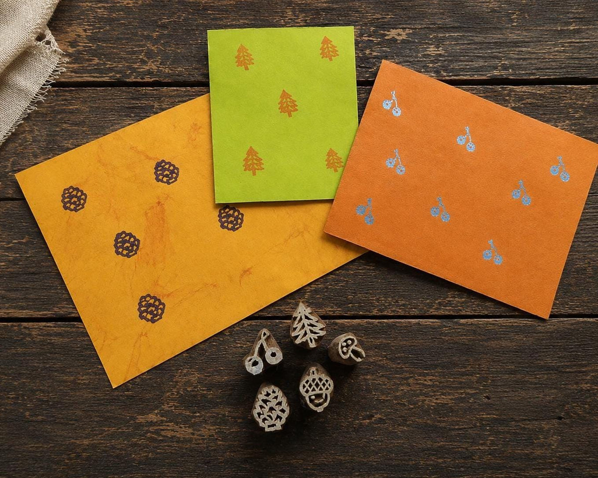 Set of five tiny hand carved Indian wood printing blocks with evergreen, pinecone, mushroom, acorn and twin cherry motifs, shown with stamped paper samples