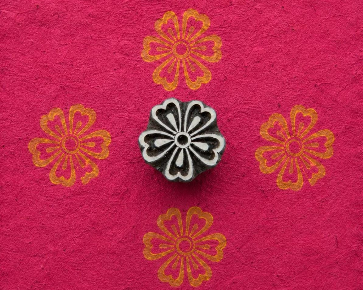 Hand carved floral wood printing block with gold flower impressions on bright pink handmade paper