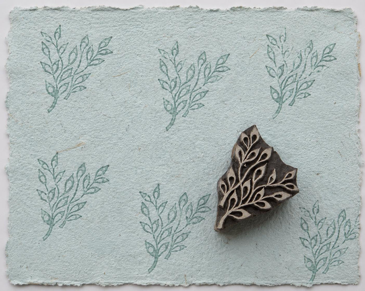 Hand carved leaf sprig wood printing block with repeated botanical impressions on pale blue handmade paper