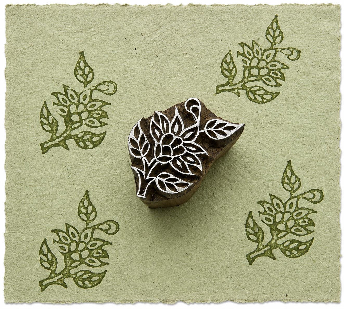 Hand carved botanical leaf wood printing block with repeated floral leaf impressions on handmade sage green paper