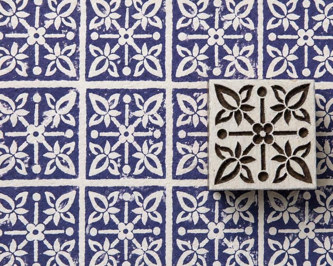 Hand carved floral tile wood stamp with four botanical flowers around a central flower, shown on handmade paper with repeated indigo impressions.