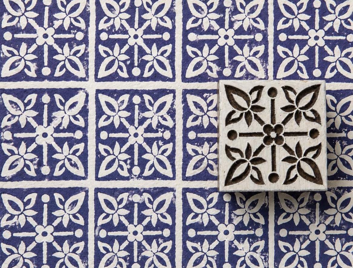 Hand carved floral tile wood stamp with four botanical flowers around a central flower, shown on handmade paper with repeated indigo impressions.