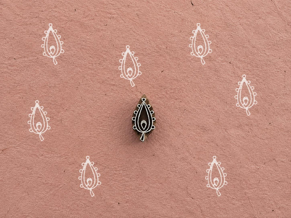 Hand carved Beaded Paisley wooden printing block with repeated paisley impressions on textured dusty pink handmade paper