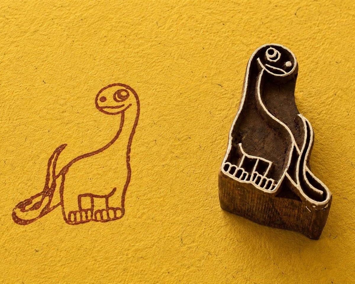 Hand carved Happy Brontosaurus wooden printing block shown beside its dinosaur print on textured yellow handmade paper