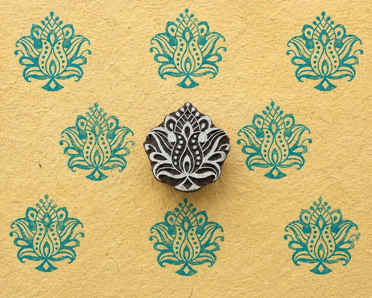 Hand carved ornate lotus wood stamp shown on handmade paper with repeated turquoise lotus impressions.