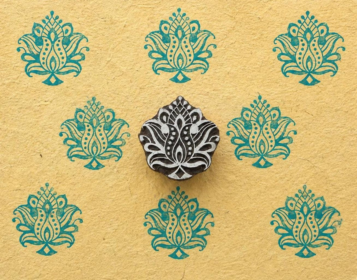Hand carved ornate lotus wood stamp shown on handmade paper with repeated turquoise lotus impressions.