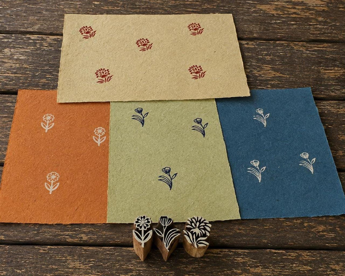 Set of three hand carved Indian wooden printing blocks with different floral designs and hand printed flower patterns on coloured handmade paper.