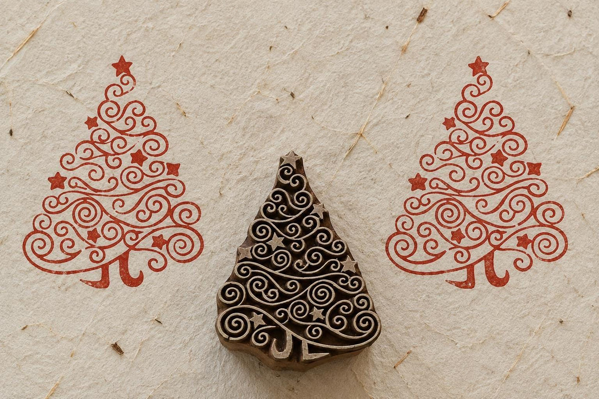 Hand carved wooden Christmas tree printing block with swirling branches and stars, shown between two red printed impressions on textured handmade paper.