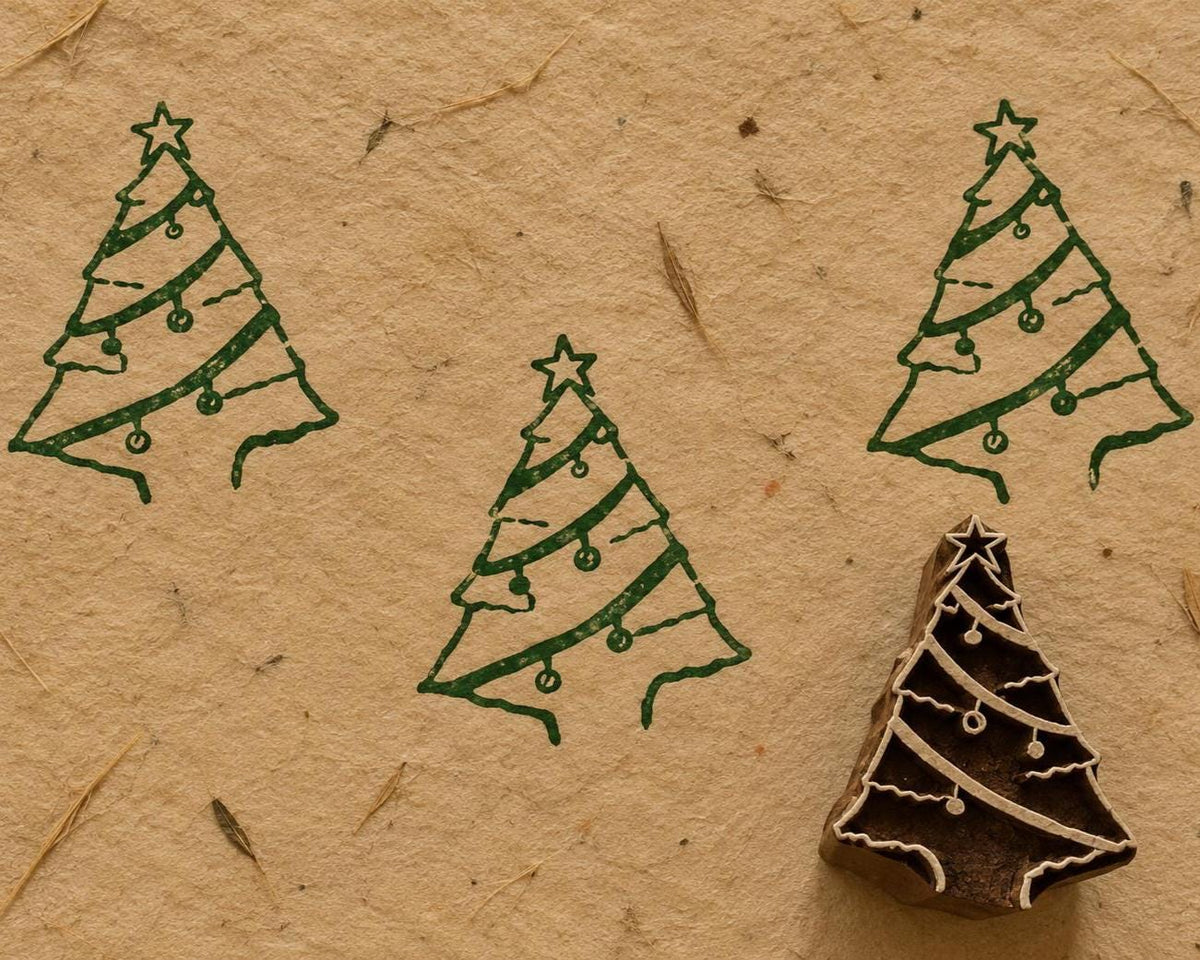 Hand carved ribbon Christmas tree wooden printing block surrounded by green Christmas tree prints on handmade paper