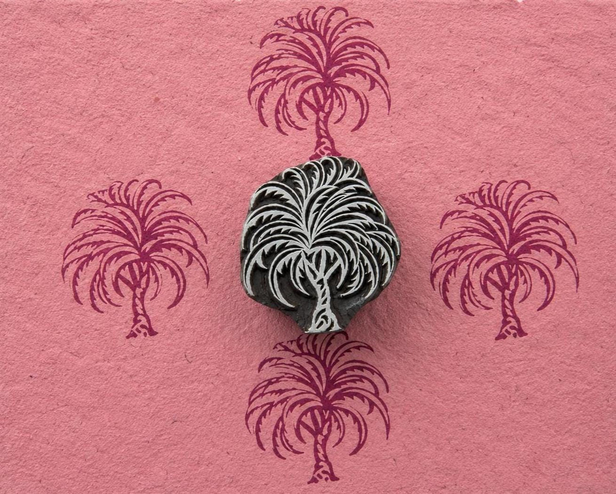 Hand carved palm tree wood printing block shown on pink handmade paper with repeated tropical palm tree impressions