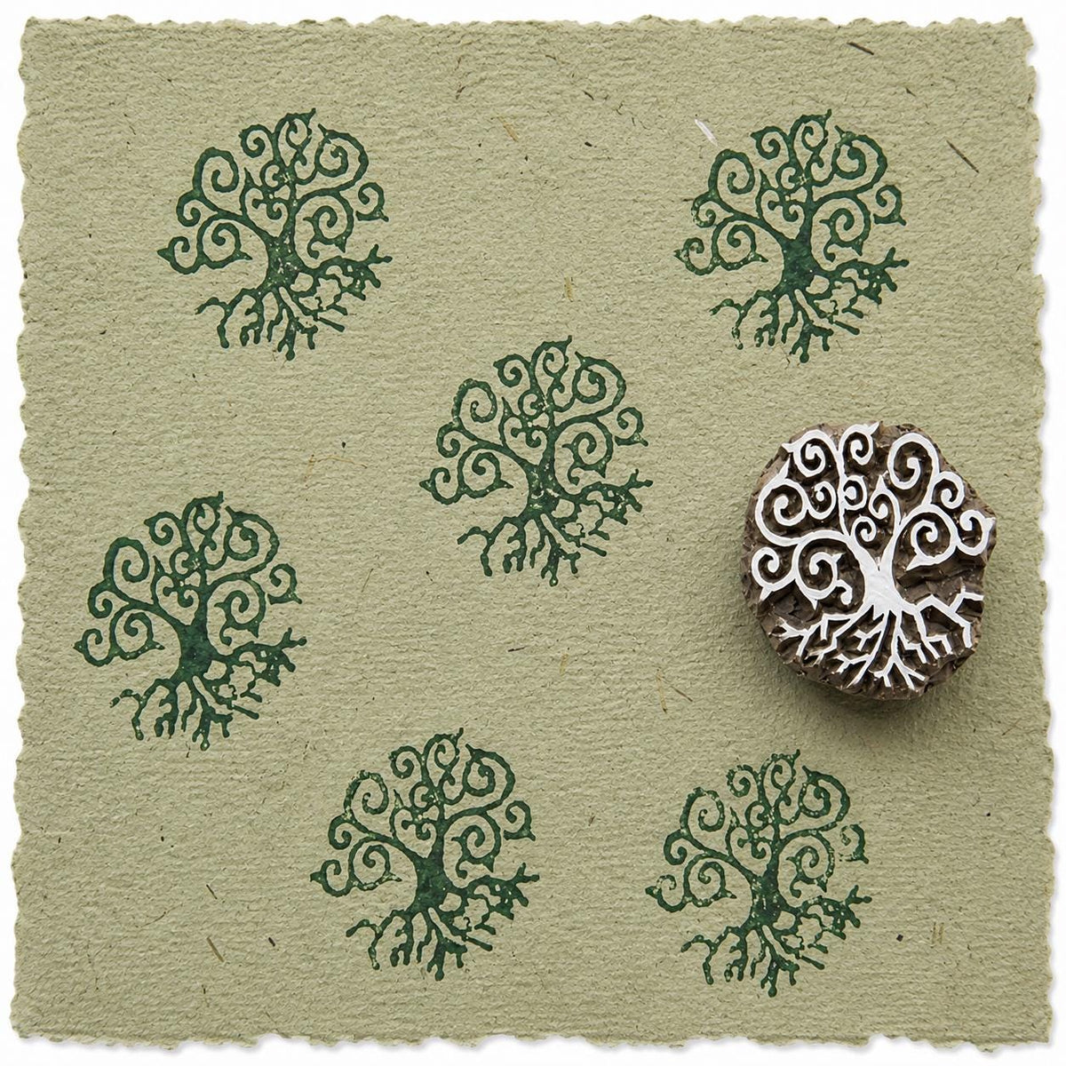 Hand carved Tree of Life wooden printing block shown with repeated green botanical impressions on handmade paper