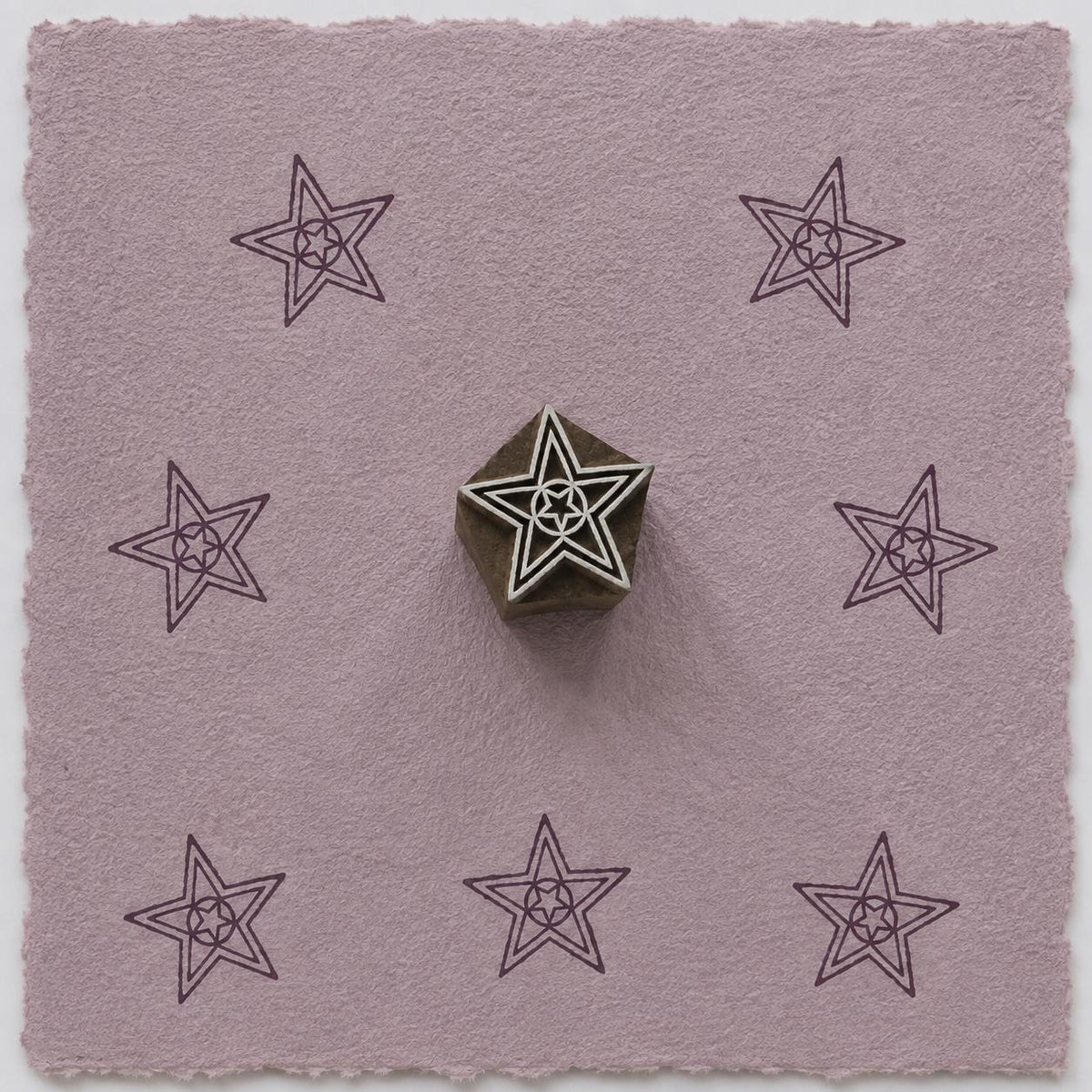 Hand carved geometric star wooden printing block with repeated star impressions on handmade paper