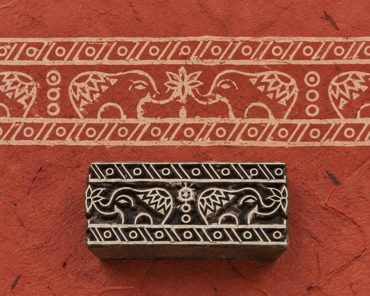 Hand carved Indian wooden printing block featuring two decorative elephants facing each other with a floral motif and geometric border bands, shown with a printed border on handmade paper.