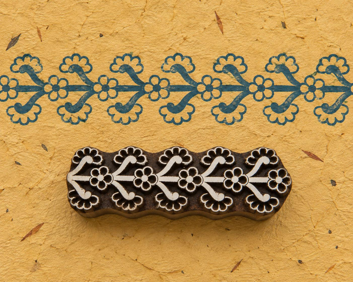 Hand carved Indian wooden printing block with a repeating floral border design, shown beside a continuous blue impression on handmade paper.