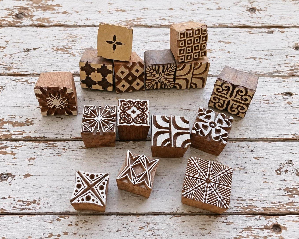 Set of 15 hand carved Indian wooden printing blocks with geometric, floral and decorative designs arranged on a distressed white wooden surface