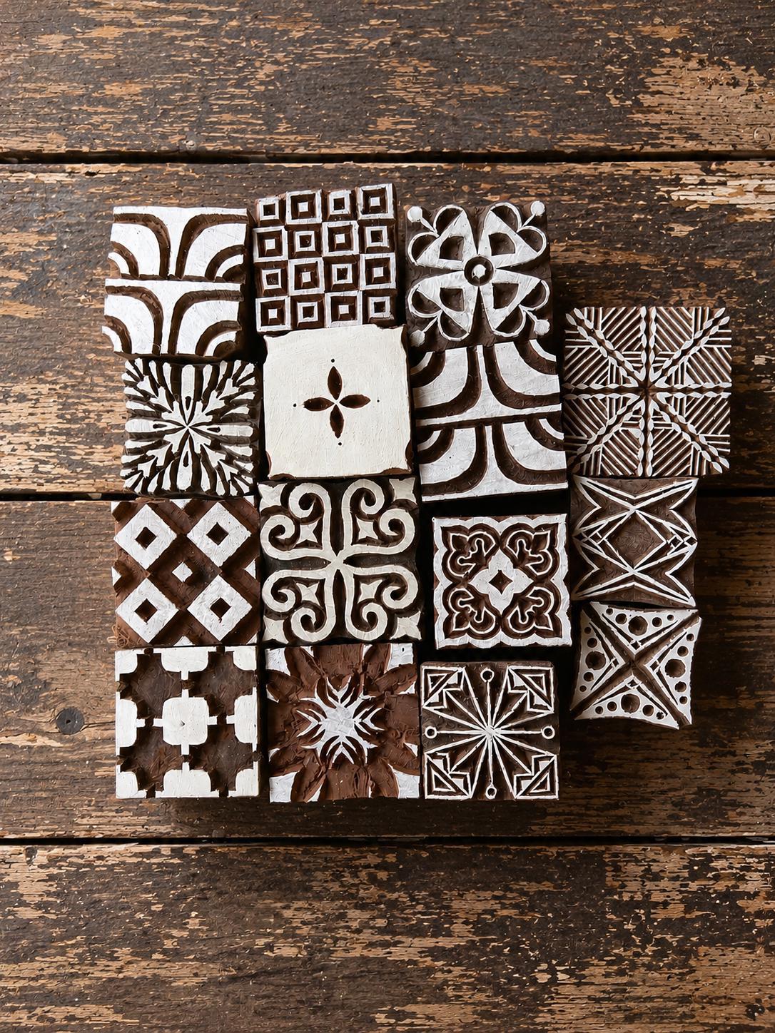 Set of 15 hand carved Indian wooden printing blocks with geometric, floral and decorative designs arranged in a group on a wooden surface