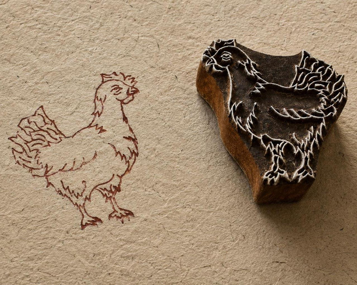 Hand-carved wooden rooster printing block shown beside its printed rooster impression on textured handmade paper