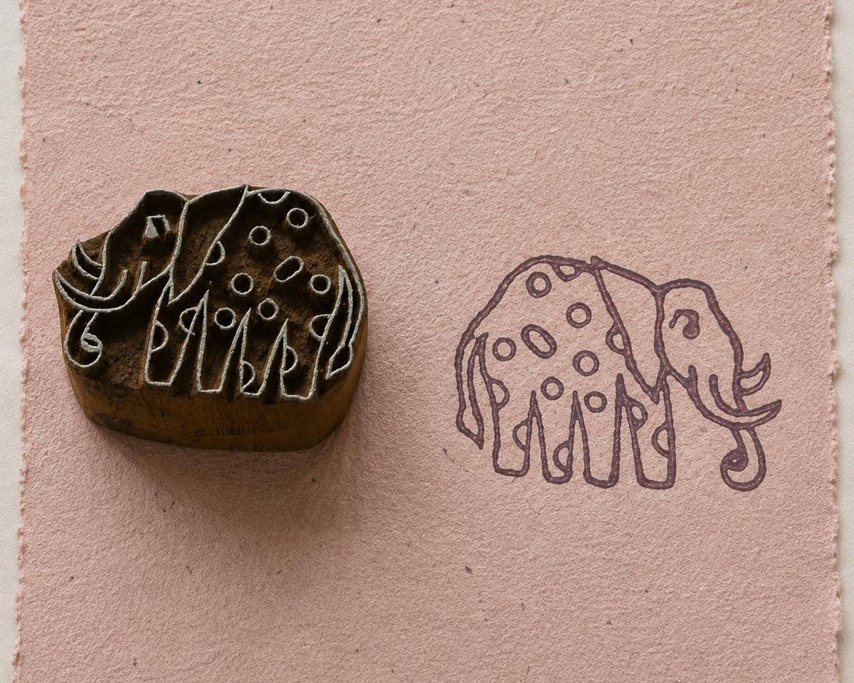 Hand carved spotted elephant wooden printing block beside its printed elephant design on textured pink handmade paper
