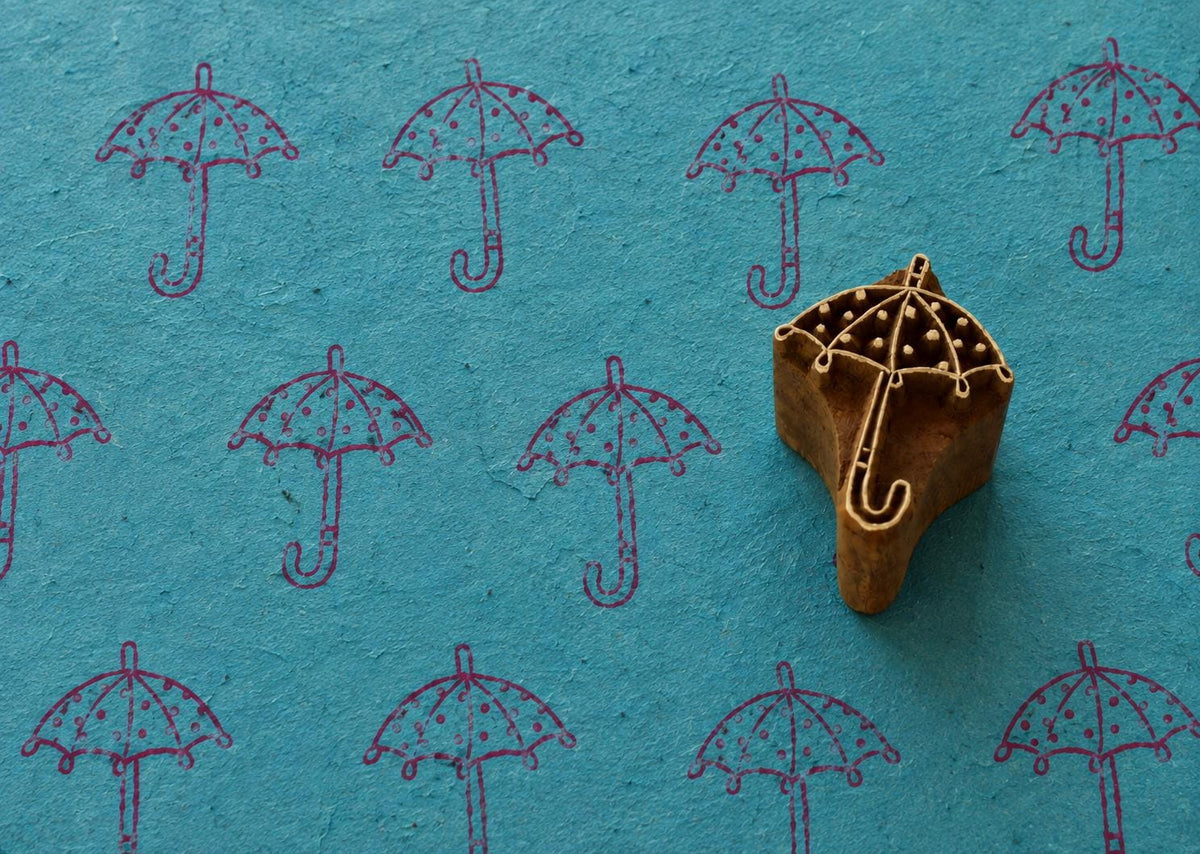 Hand carved Raindrop Umbrella wooden printing block with repeated umbrella impressions on textured teal handmade paper