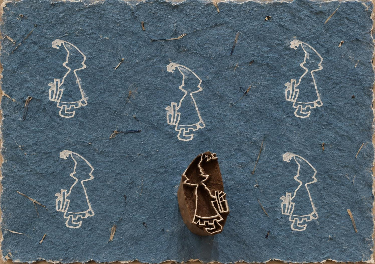 Wooden Christmas printing block featuring a little girl carrying a wrapped Christmas gift, shown with repeated white prints.