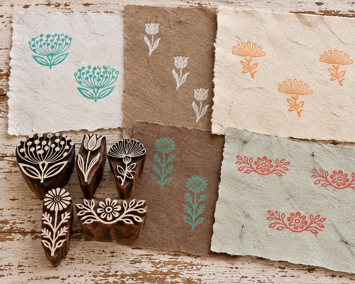 Five hand-carved wooden floral printing blocks with flower and border designs shown with colorful handmade paper prints