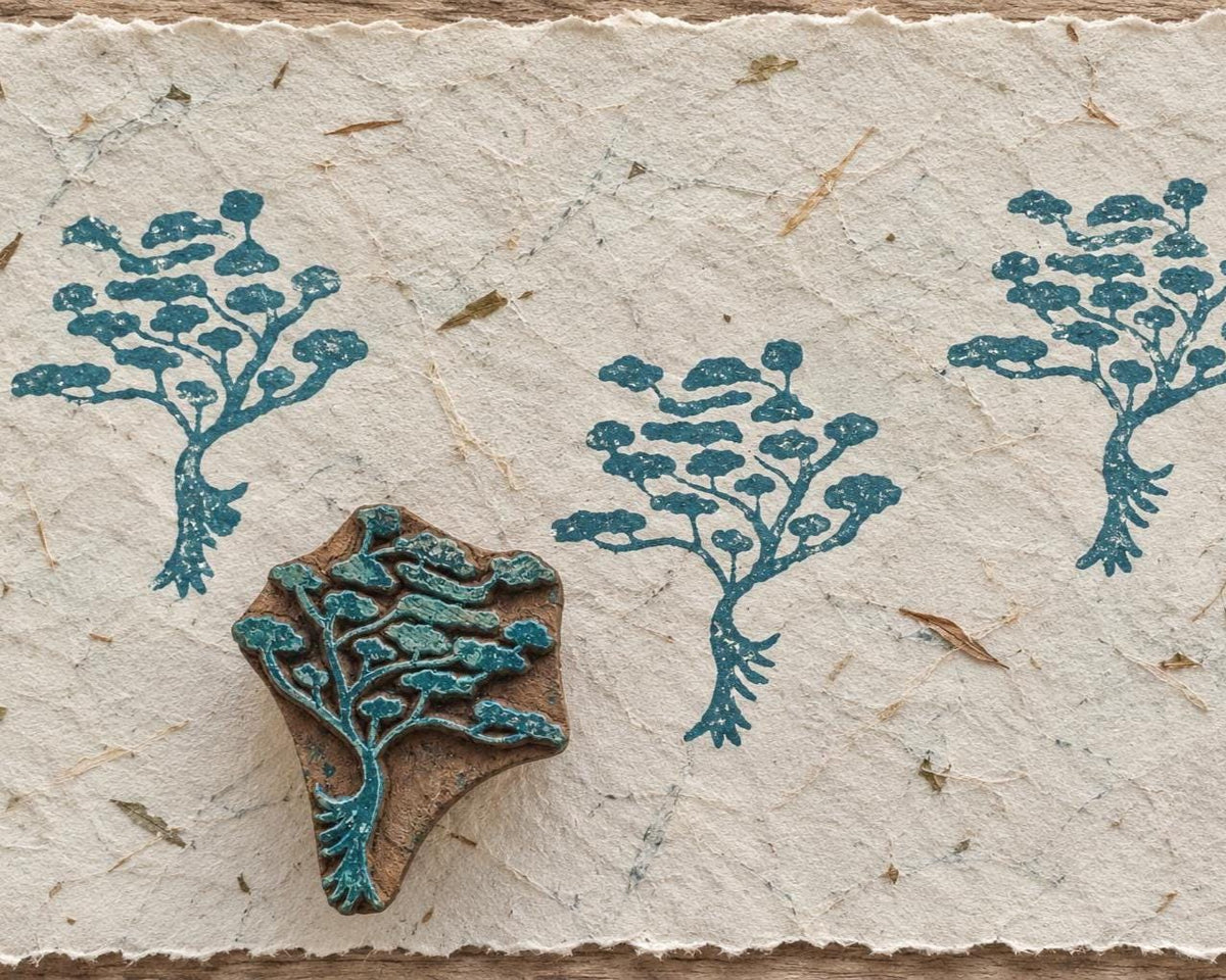 Hand carved wooden Rooted Tree printing block with blue-green tree impressions on textured handmade paper.
