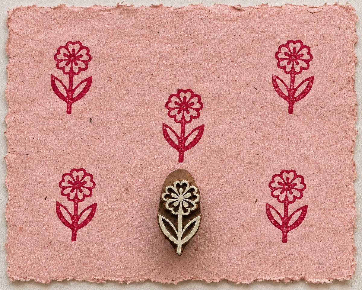 Hand carved wooden Daisy Stem printing block with repeated burgundy floral impressions on pink handmade paper.