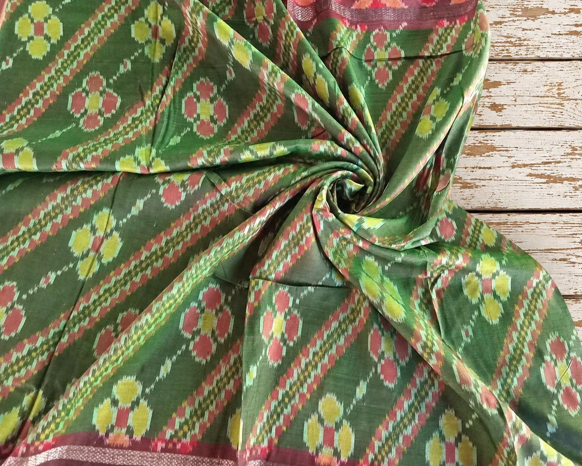 Close-up of vintage green Indian silk showing the detailed ikat-style geometric floral pattern in red yellow and green