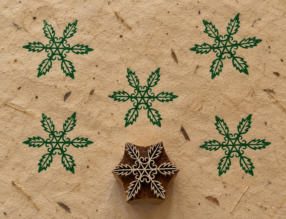 Wooden Christmas printing block with an intricate six-point snowflake made from leafy botanical motifs, shown with green prints.