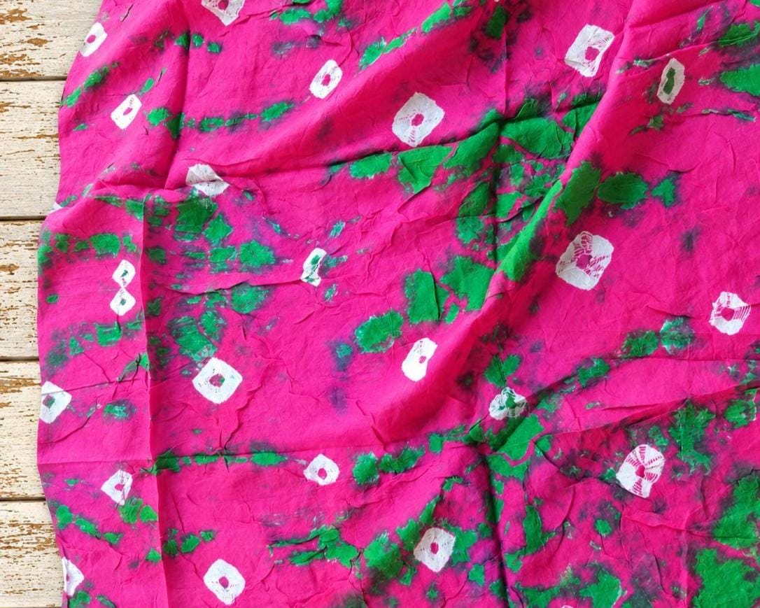 Pink and green vintage sari textile with scattered white motifs and varied tie-dye markings, spread out to show the pattern.