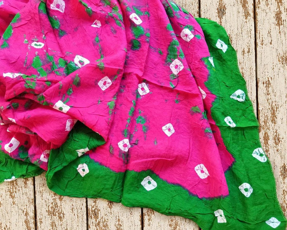 Bright pink vintage sari fabric with green tie-dye patches and white motifs, displaying the distinctive colours and pattern.