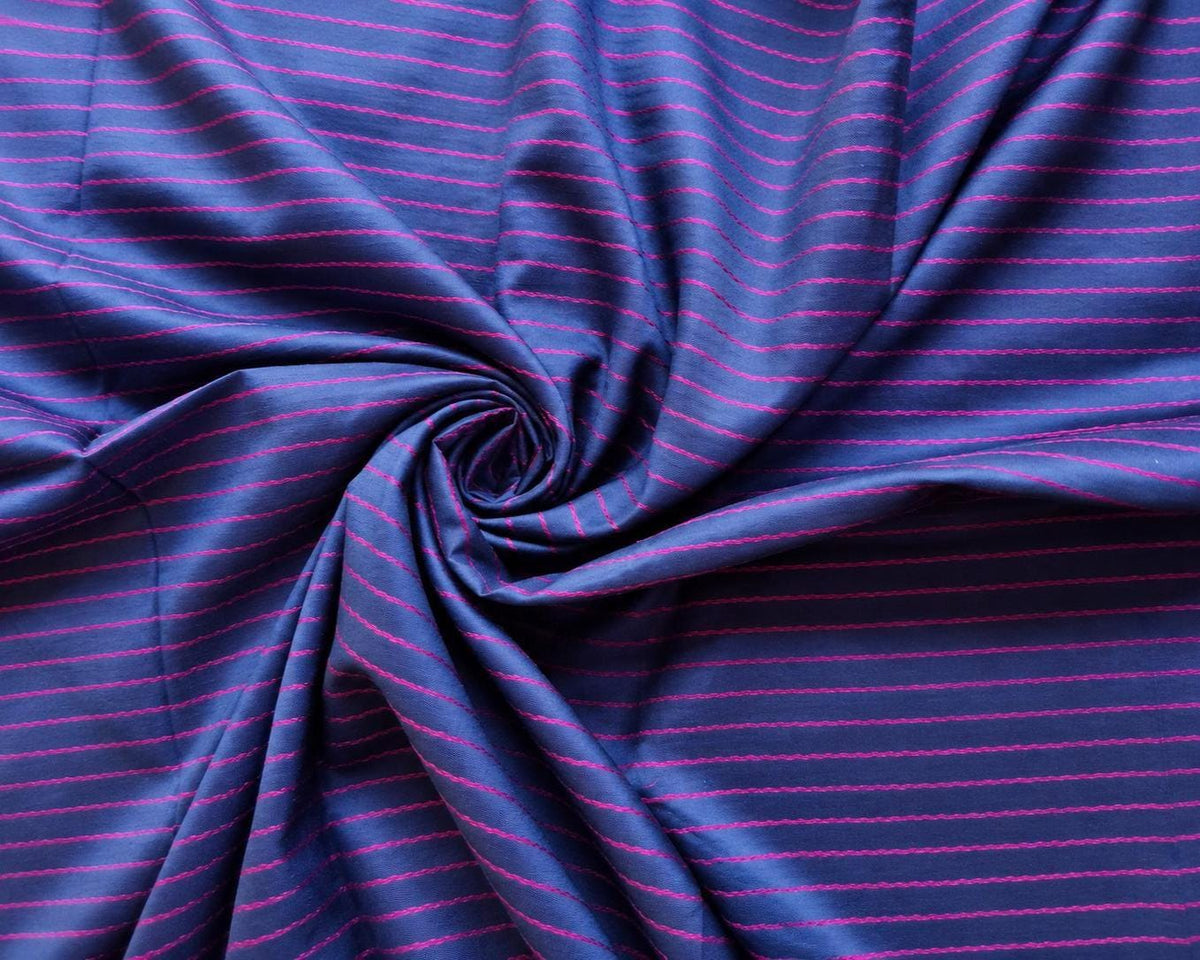 Close-up of soft blue-purple sari fabric arranged in folds, showing fine magenta stripes and the sheen of the textile.