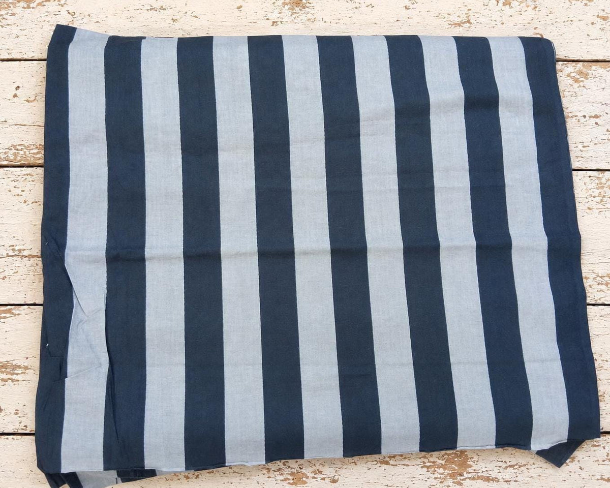 Folded cotton fabric with wide navy and light blue stripes on a distressed white wooden surface.
