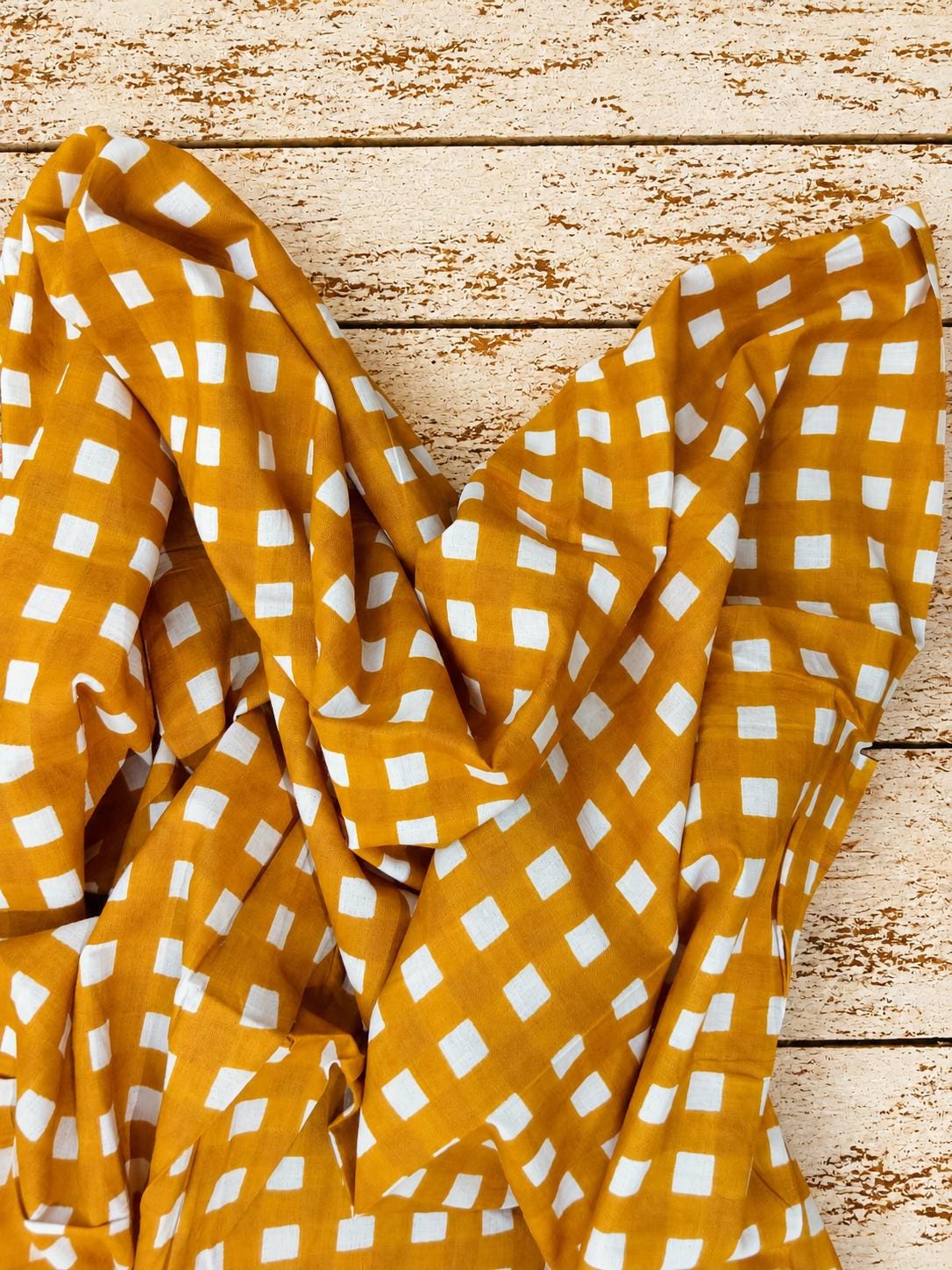 Golden mustard fabric with white checks draped across a rustic wooden surface.