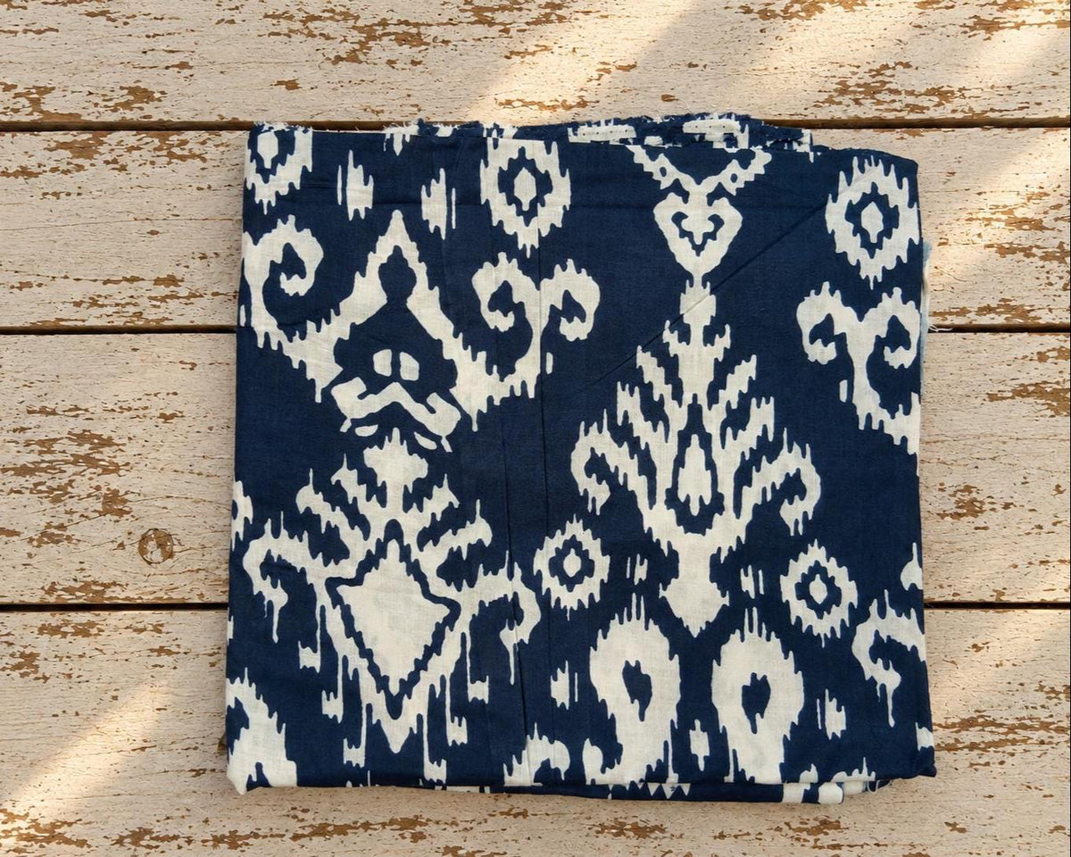 Folded navy blue and cream cotton fabric featuring a bold all-over ikat-inspired print.