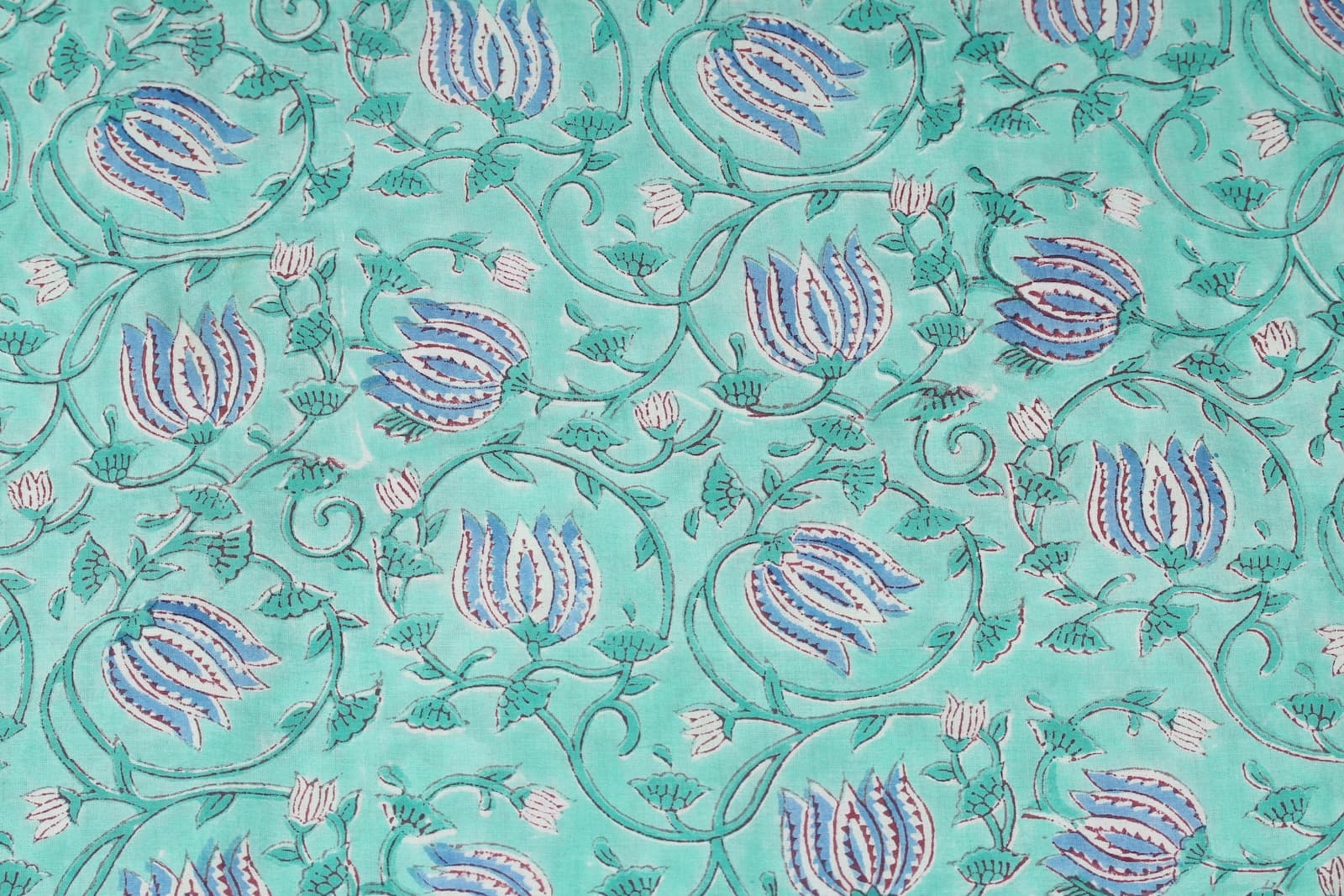 Close-up of blue lotus flower buds and delicate vine motifs on aqua block printed cotton fabric