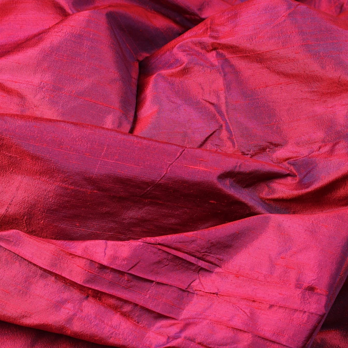 Magenta Orchid dupion silk fabric folded on a rustic tabletop showing iridescent magenta silk yardage and natural slub texture