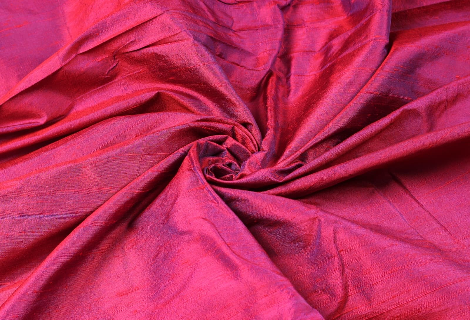 Magenta Orchid dupion silk fabric arranged in a swirl highlighting magenta and orchid colour shifts with natural silk texture