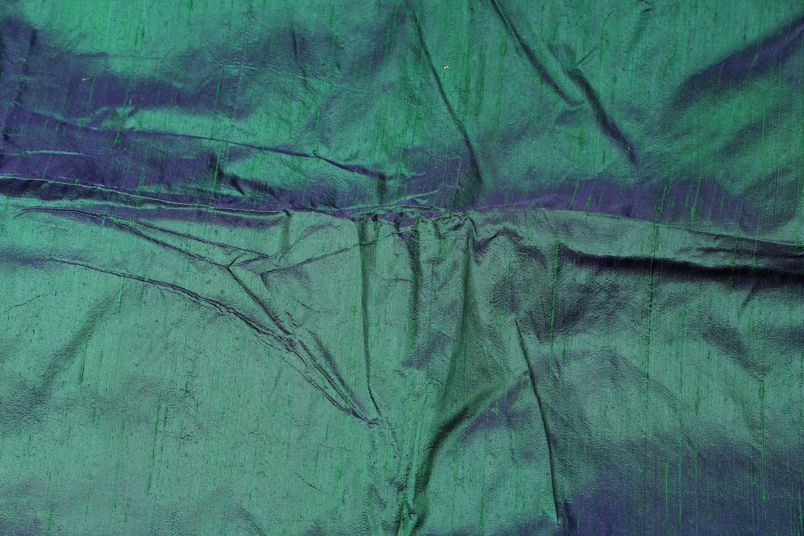 Peacock Lagoon dupion silk fabric draped to display iridescent blue-green sheen, natural slubs, and luxurious raw silk texture