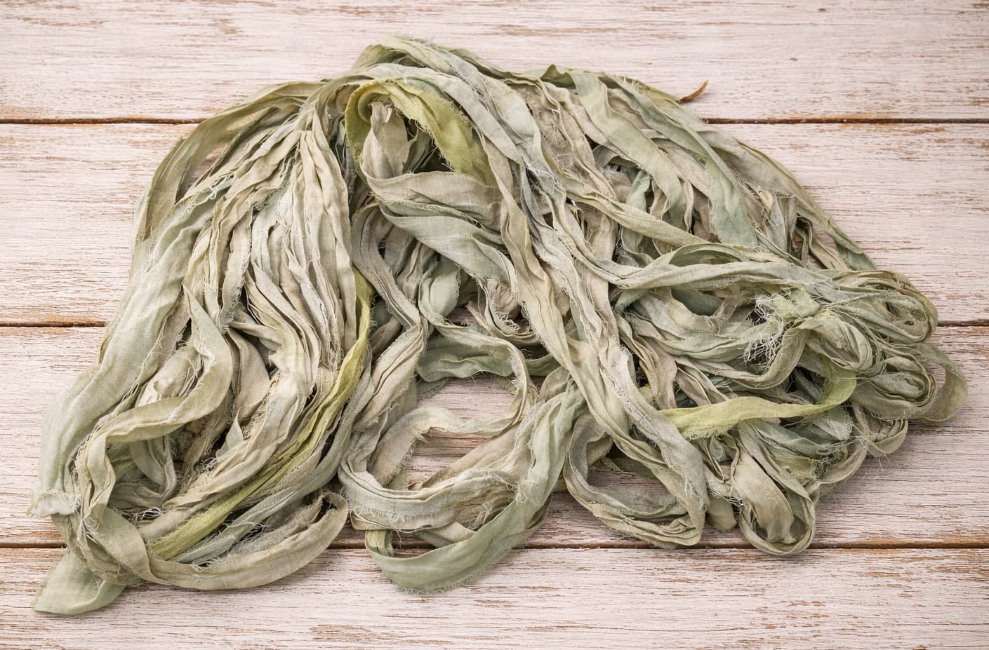 Flat lay of Faded Sage sari silk ribbon showing natural tonal variation and textured silk strands.