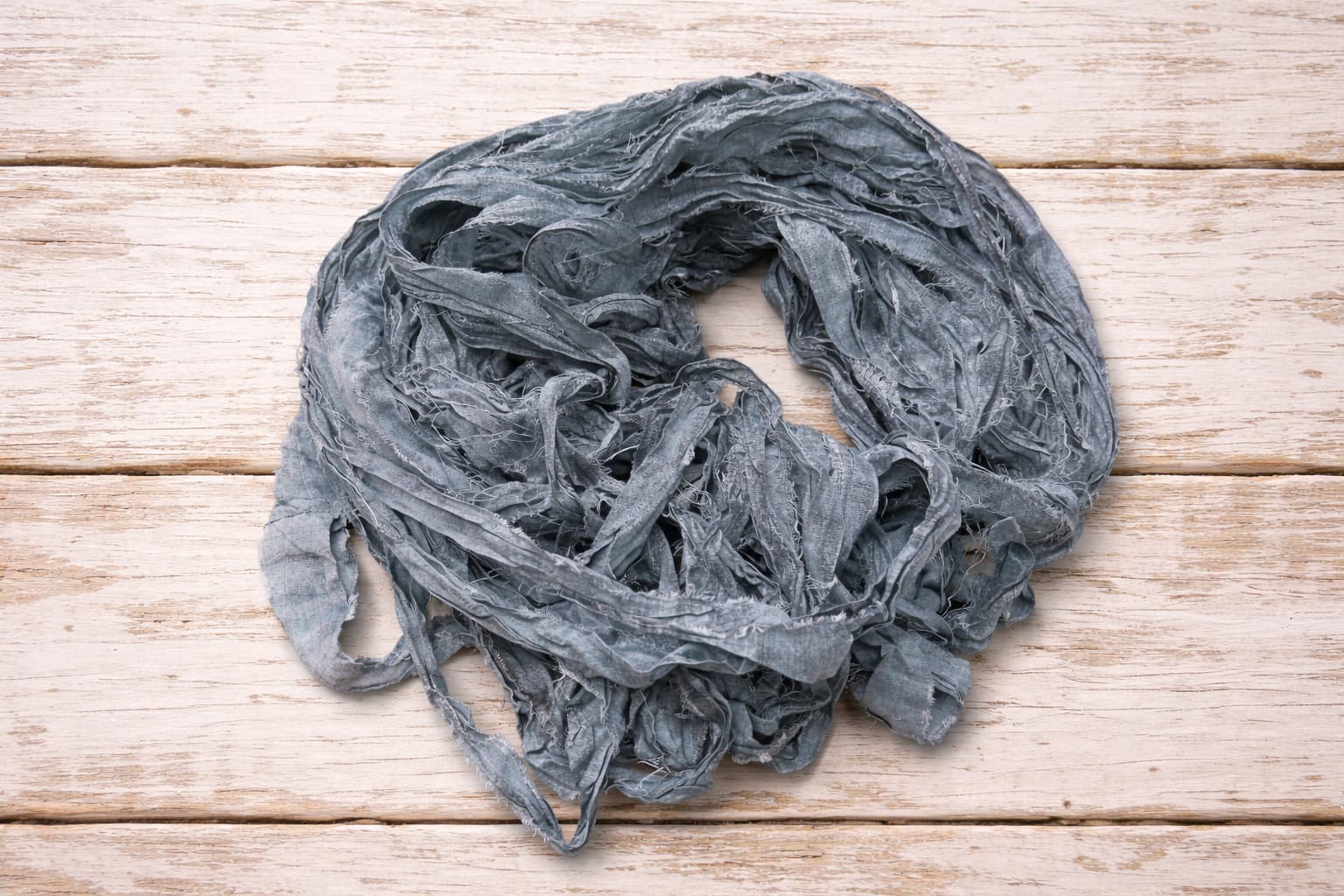 Loose hank of storm grey sari silk ribbon made from reclaimed sari silk fabric.